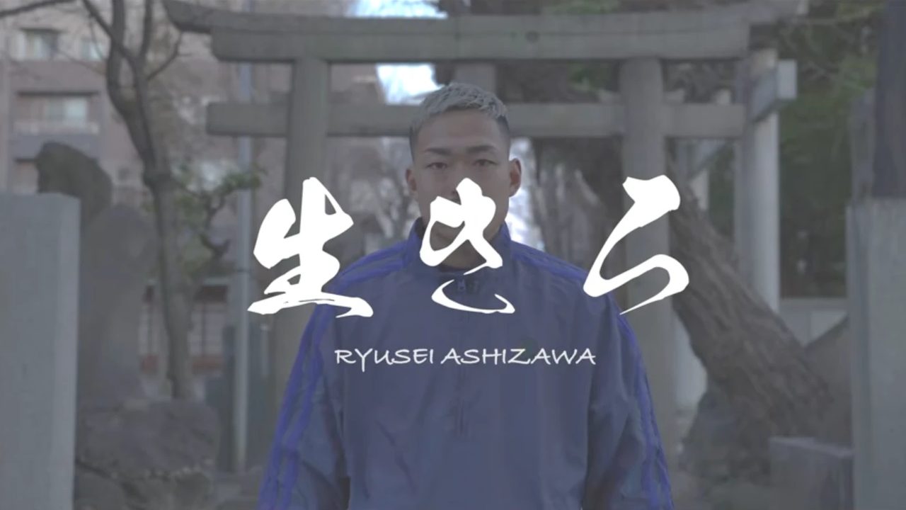 鳥居の前に立つ芦澤竜誠さんと「生きろ」の文字