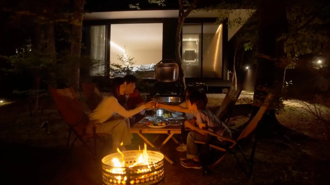 夜の森のヴィラで焚き火を囲んで乾杯する家族